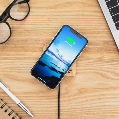Handcrafted wooden wireless charger with smartphone displaying charging status on a workspace desk.